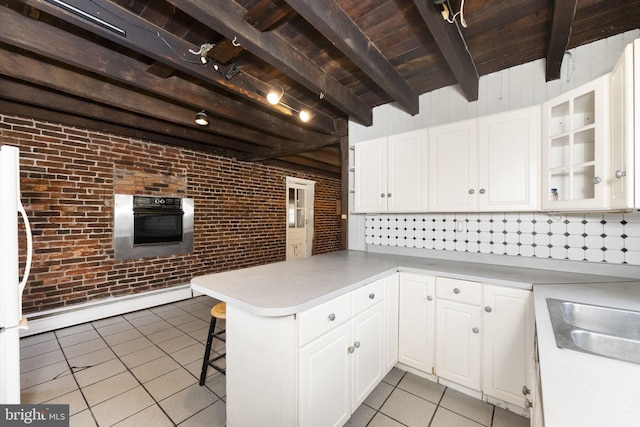 kitchen with brick wall, oven, light tile patterned floors, beam ceiling, and white cabinets