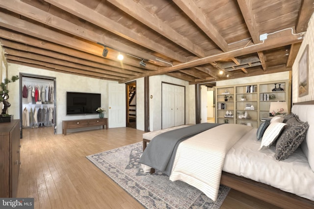 bedroom with beam ceiling, a spacious closet, hardwood / wood-style floors, and rail lighting