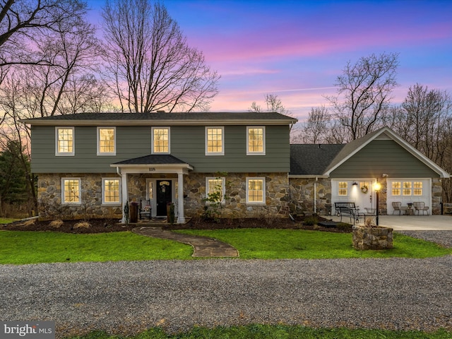 colonial home with gravel driveway, stone siding, and a front lawn