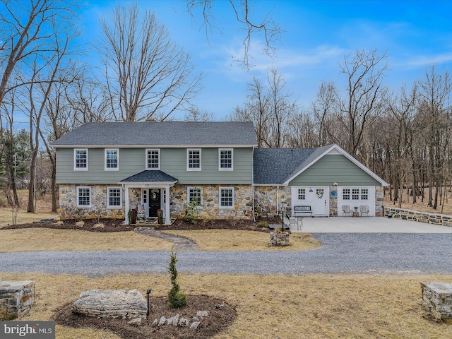 colonial house featuring stone siding, roof with shingles, and driveway