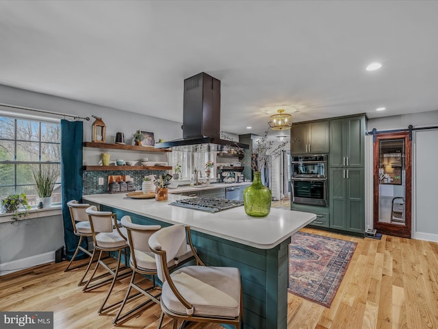 kitchen featuring open shelves, green cabinets, a barn door, appliances with stainless steel finishes, and island range hood