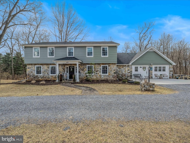 colonial inspired home with a garage, stone siding, and driveway