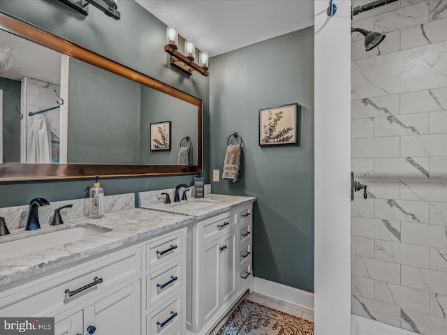 full bath with a sink, double vanity, baseboards, and tiled shower