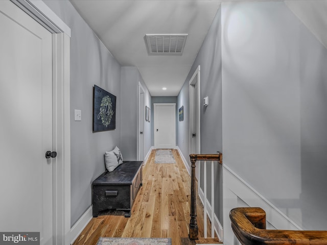 hallway featuring light wood finished floors, baseboards, visible vents, and an upstairs landing