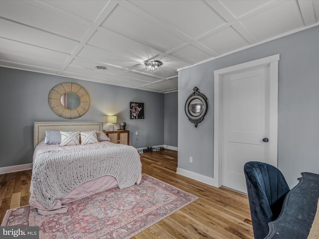 bedroom featuring coffered ceiling, visible vents, baseboards, and wood finished floors