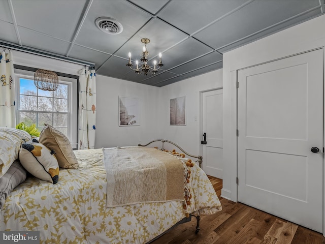 bedroom featuring a paneled ceiling, visible vents, a notable chandelier, and wood finished floors