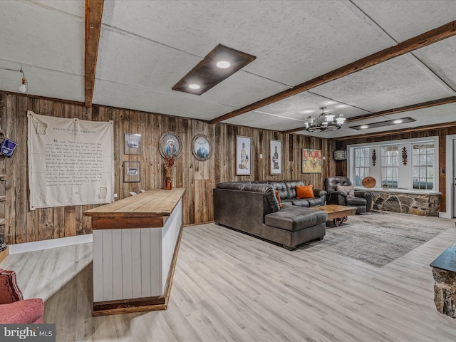 living area with a chandelier, beam ceiling, wooden walls, and light wood finished floors