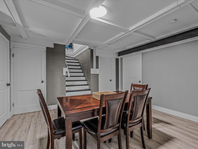 dining space with concrete block wall, stairway, light wood-type flooring, beamed ceiling, and baseboards