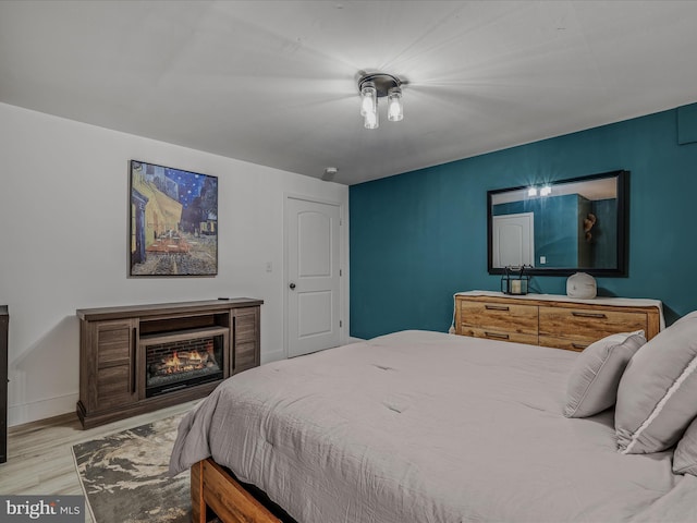 bedroom featuring a warm lit fireplace, baseboards, and wood finished floors