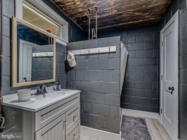 bathroom with concrete block wall, wooden ceiling, vanity, and wood finished floors