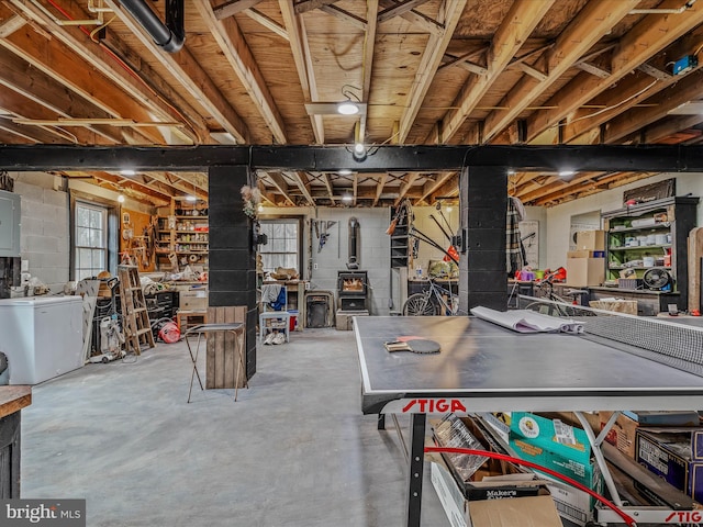 below grade area featuring electric panel, concrete block wall, a wood stove, and refrigerator