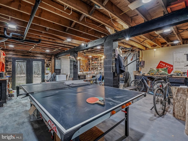 rec room with concrete block wall, electric panel, concrete flooring, and french doors