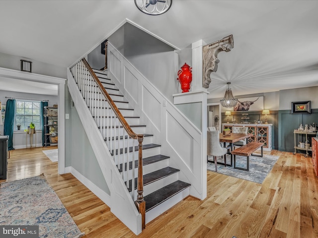 staircase featuring a chandelier, a wainscoted wall, a decorative wall, and wood finished floors