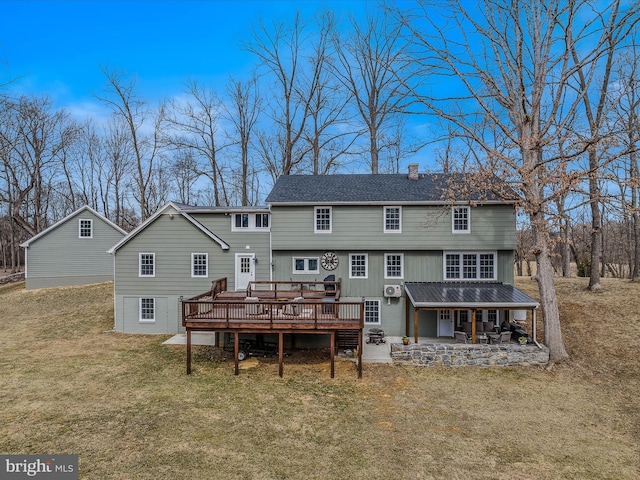 rear view of house with a deck, a patio, a shingled roof, a yard, and a chimney