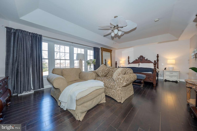 bedroom with a tray ceiling, dark wood-style flooring, and baseboards