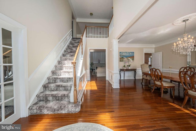 entrance foyer featuring crown molding, stairway, ornate columns, and an inviting chandelier