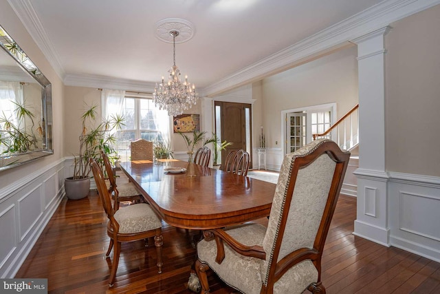 dining space with a decorative wall, ornamental molding, dark wood-style floors, decorative columns, and an inviting chandelier