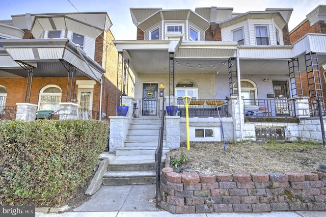 townhome / multi-family property featuring covered porch, brick siding, and stairs