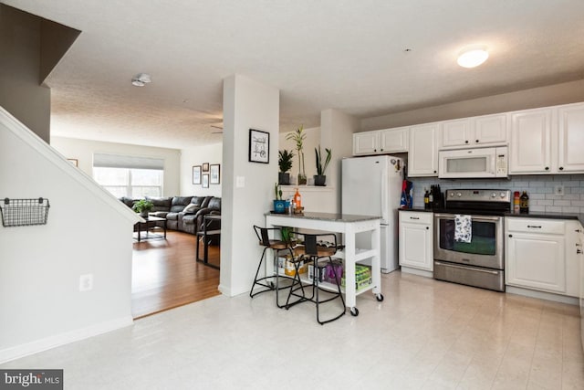 kitchen with white appliances, white cabinets, dark countertops, open floor plan, and backsplash