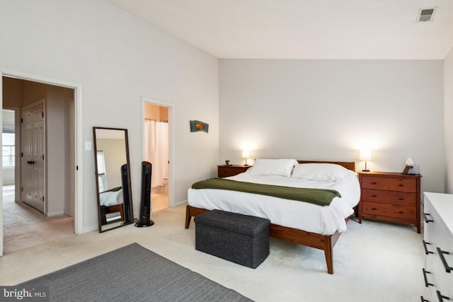 bedroom featuring visible vents, light carpet, high vaulted ceiling, ensuite bath, and baseboards