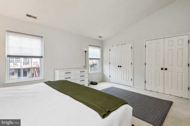 bedroom featuring lofted ceiling, carpet flooring, visible vents, and multiple closets