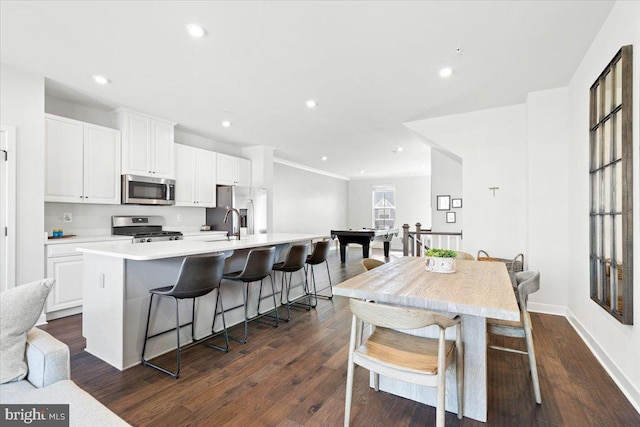 kitchen featuring white cabinetry, stainless steel appliances, an island with sink, and dark wood-style flooring