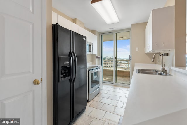 kitchen featuring stainless steel appliances, a sink, white cabinets, light countertops, and expansive windows