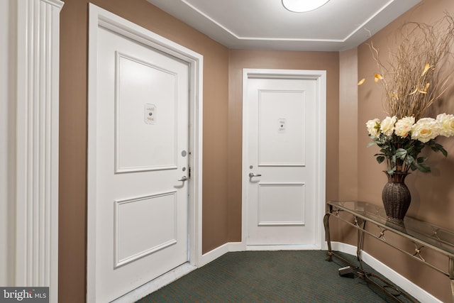 doorway featuring dark carpet and baseboards