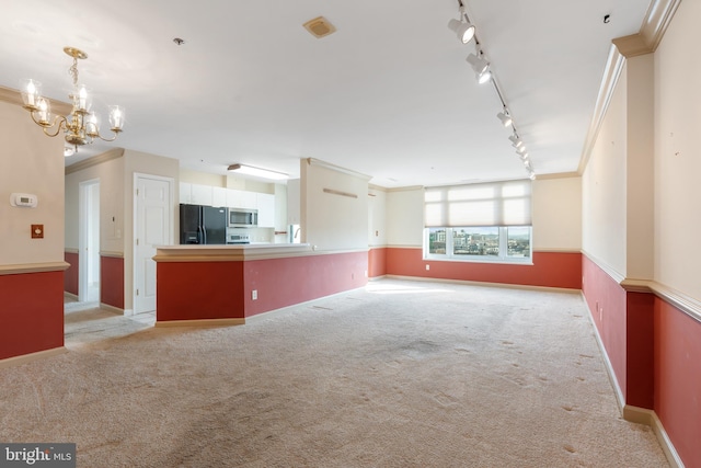 unfurnished living room featuring light carpet, baseboards, ornamental molding, rail lighting, and an inviting chandelier