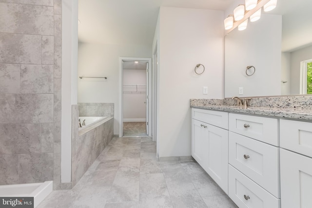 bathroom with a walk in closet, a garden tub, vanity, and baseboards