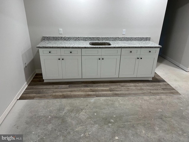 kitchen with a sink, baseboards, and light stone counters