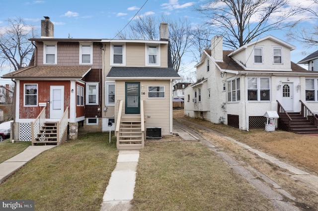 view of front of property with entry steps, roof with shingles, a front lawn, and a chimney