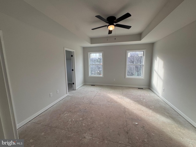 spare room featuring a raised ceiling, ceiling fan, and baseboards