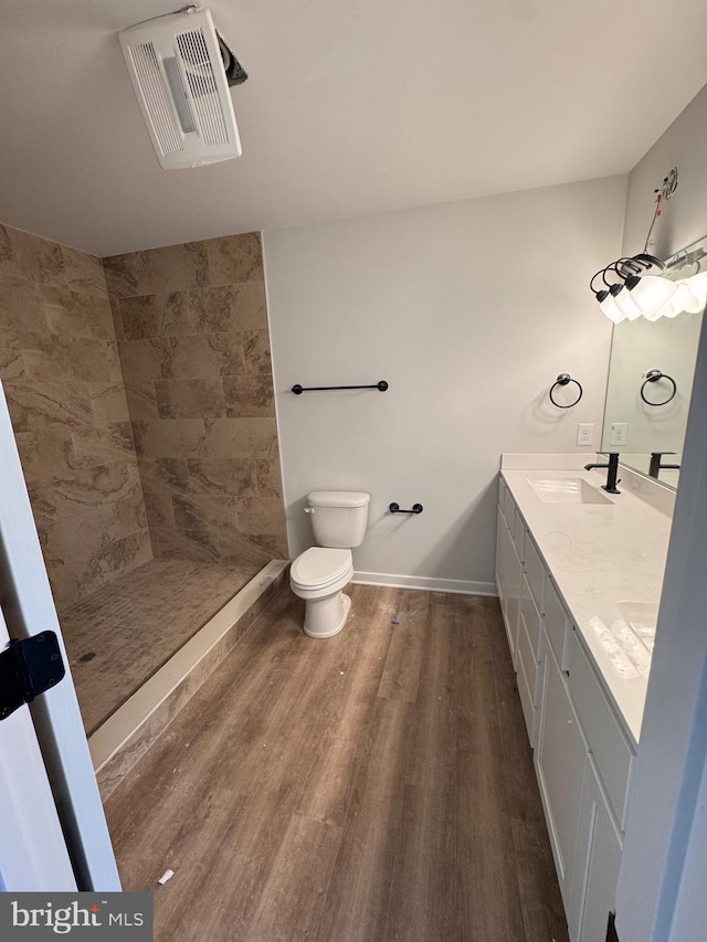 bathroom featuring visible vents, toilet, wood finished floors, a tile shower, and a sink