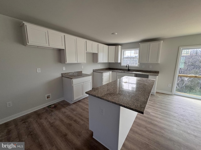 kitchen with wood finished floors, dark stone countertops, a kitchen island, and white cabinetry