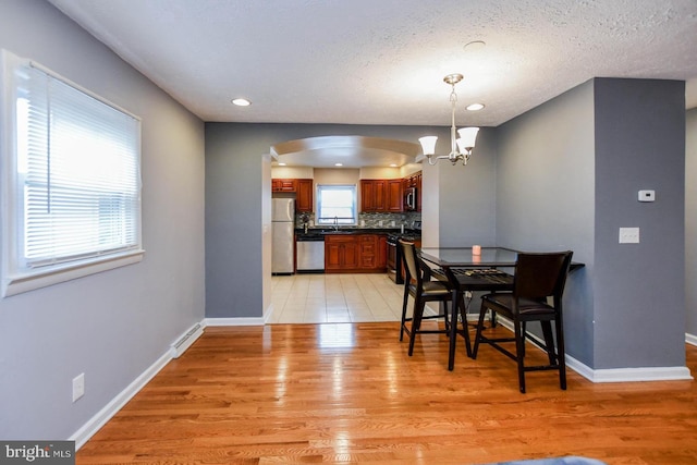 dining room with light wood-type flooring, an inviting chandelier, baseboards, and arched walkways