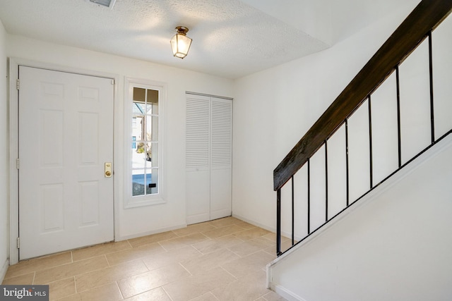 foyer entrance featuring visible vents, baseboards, stairway, and a textured ceiling