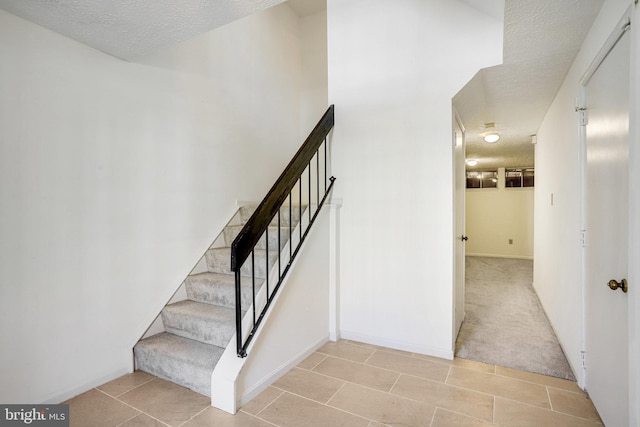 staircase featuring a textured ceiling, baseboards, carpet flooring, and tile patterned floors