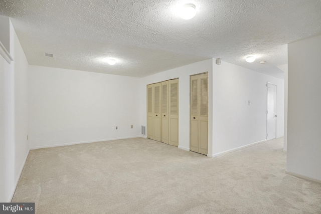 basement featuring a textured ceiling, visible vents, and light colored carpet