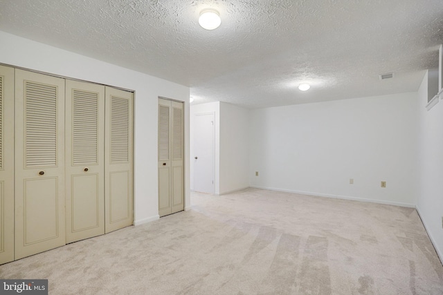 unfurnished bedroom with two closets, visible vents, carpet flooring, a textured ceiling, and baseboards