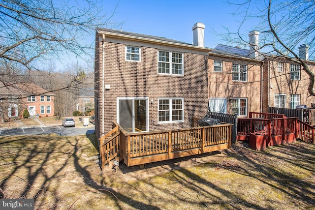 rear view of house with a chimney, brick siding, a yard, and a deck