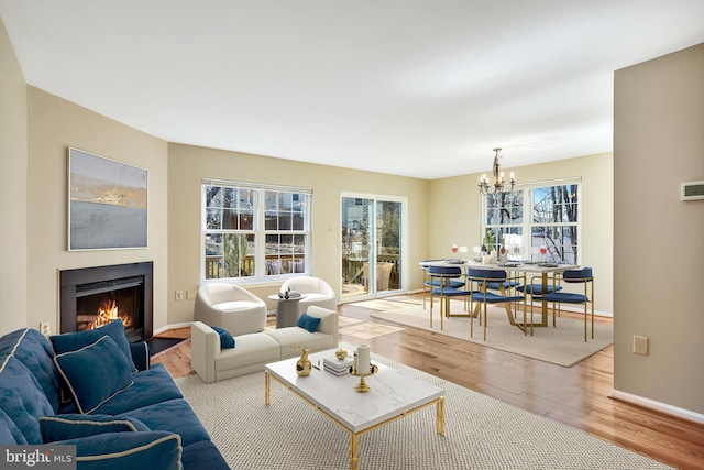 living area with a notable chandelier, a lit fireplace, baseboards, and wood finished floors