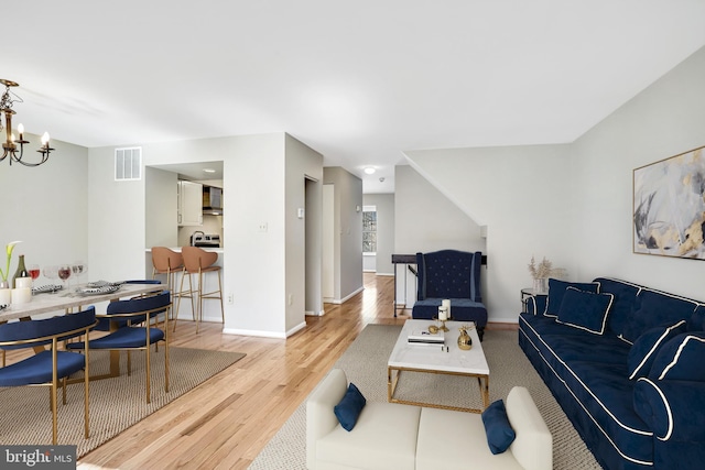 living area featuring baseboards, light wood-type flooring, visible vents, and an inviting chandelier