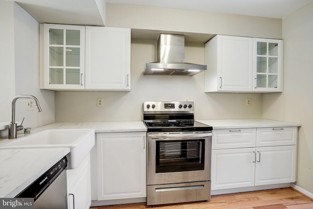 kitchen featuring appliances with stainless steel finishes, white cabinets, a sink, and wall chimney exhaust hood