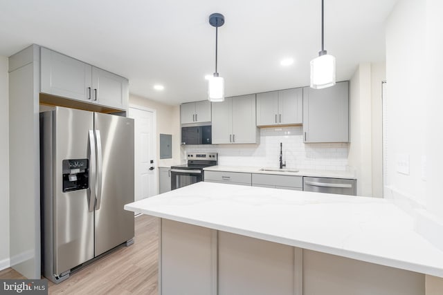 kitchen featuring stainless steel appliances, backsplash, gray cabinetry, a sink, and light stone countertops