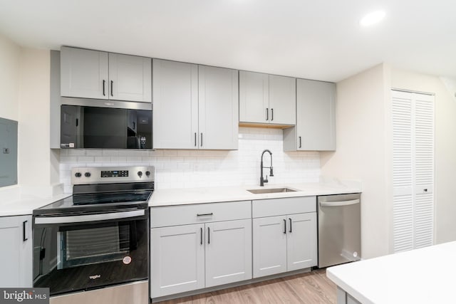 kitchen featuring stainless steel appliances, light countertops, a sink, and gray cabinetry