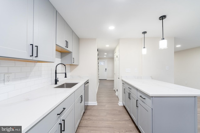 kitchen featuring light wood-style flooring, a peninsula, a sink, stainless steel dishwasher, and tasteful backsplash