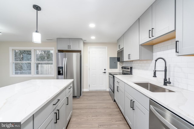 kitchen with stainless steel appliances, a sink, light wood-type flooring, backsplash, and pendant lighting