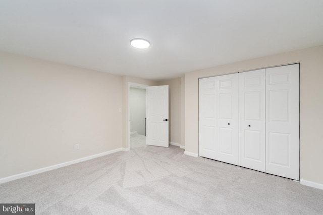 unfurnished bedroom with a closet, light colored carpet, and baseboards