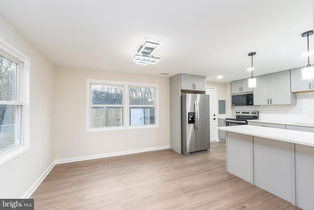 kitchen with stainless steel appliances, a healthy amount of sunlight, light wood-style floors, light countertops, and backsplash